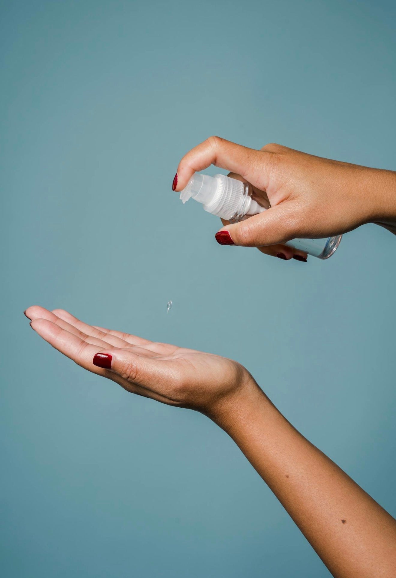 Hand holding a small bottle of clear liquid over another hand against a plain background